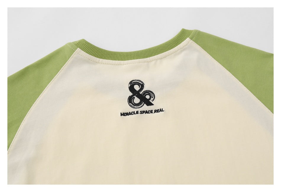 Close-up of the cream shirt back with green raglan sleeves and a small dark embroidered emblem and lettering.
