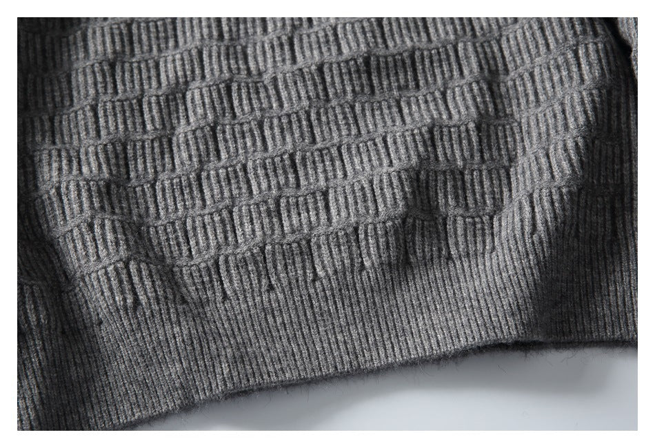 Close-up of the gray sweater's raised block-knit pattern above its wide ribbed hem.