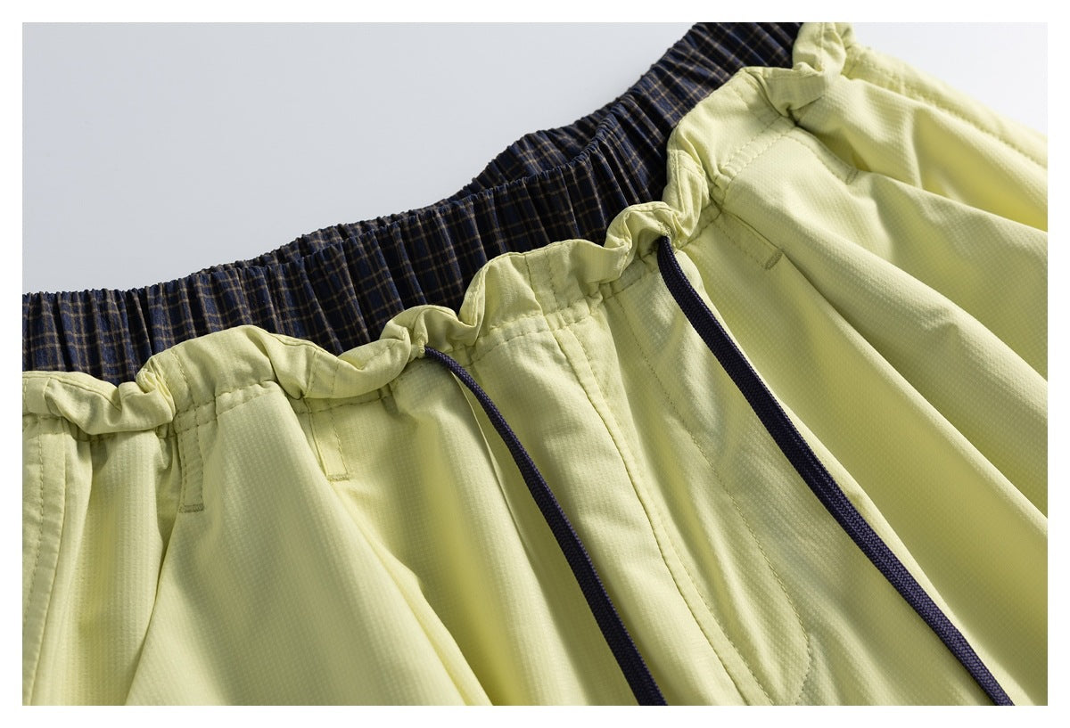 Close-up of pale yellow garment with elastic waistband, navy drawstrings, and dark plaid inner waistband.