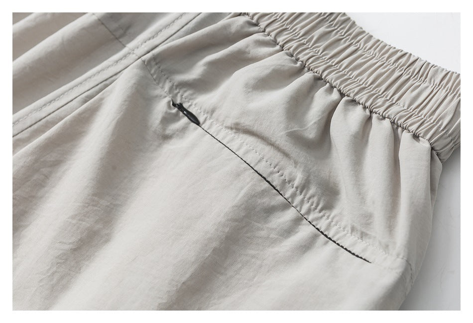 Closer view of the gathered elastic waistband and zippered pocket on light gray-beige pants.