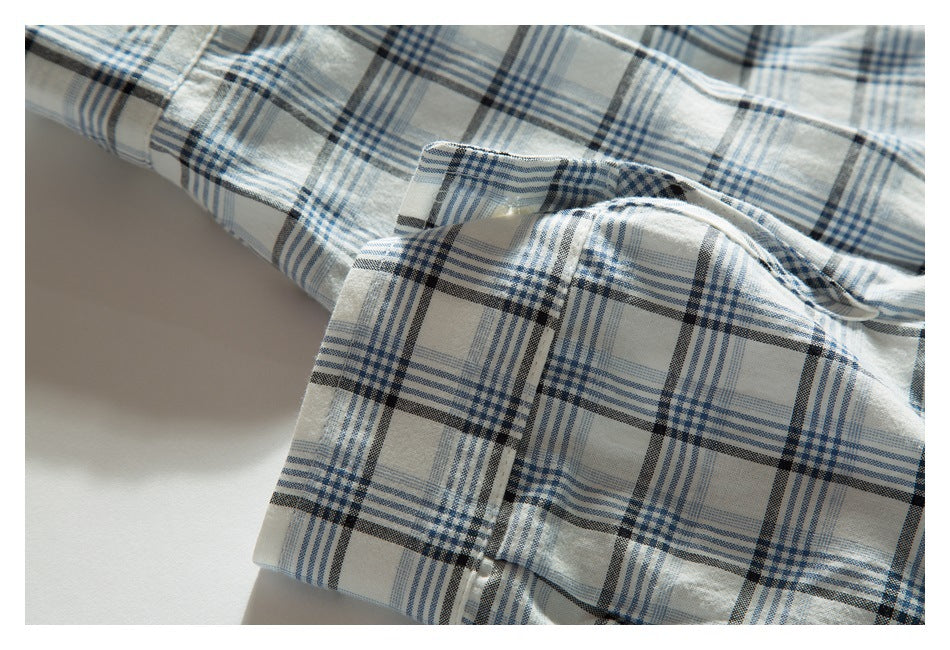 Close-up of a folded, buttoned edge on white fabric with blue and charcoal plaid.