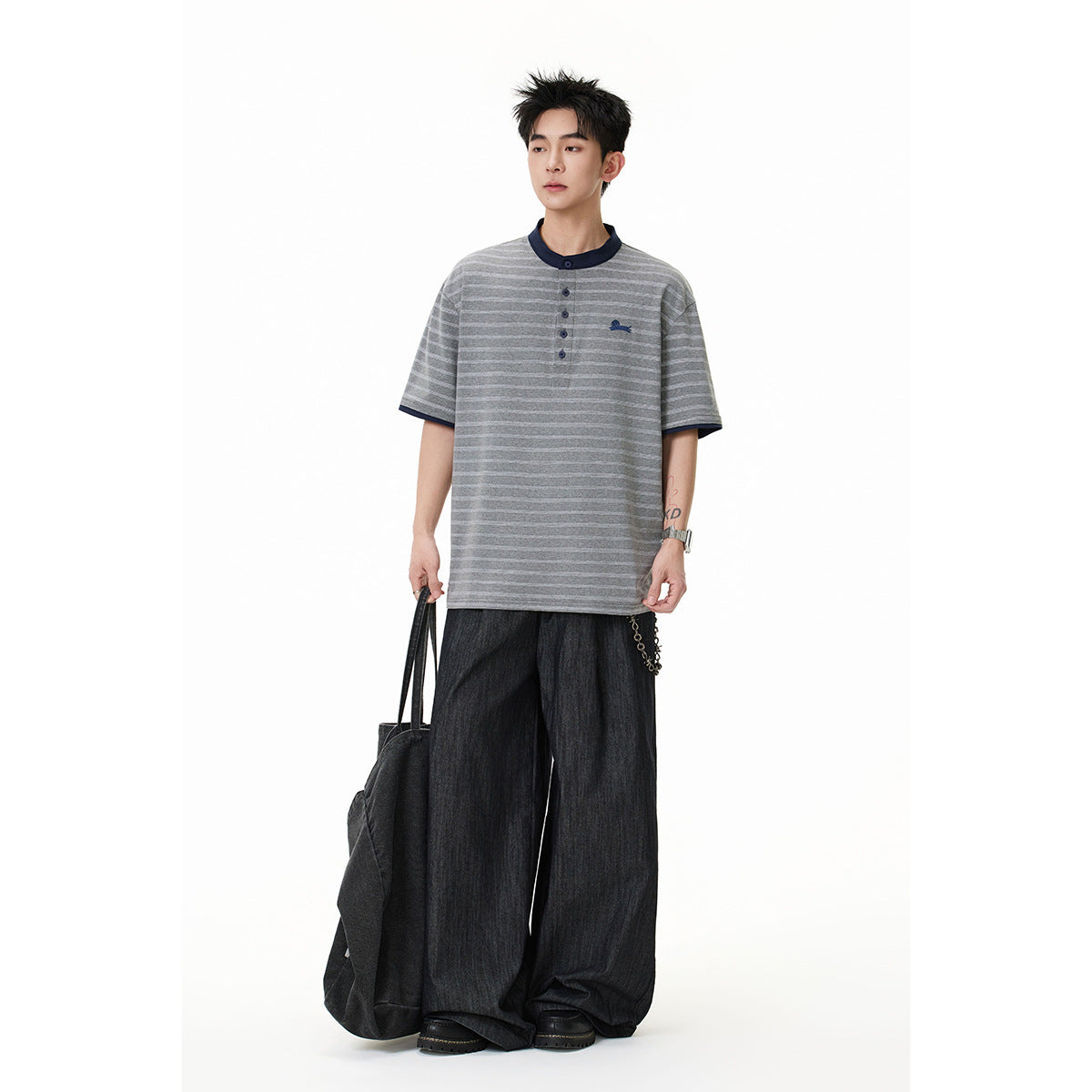 Model wearing a gray striped short-sleeve henley with navy trim and loose dark trousers.