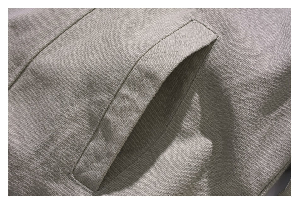 Close-up of a slanted pocket opening and stitched seams on the light gray jacket.
