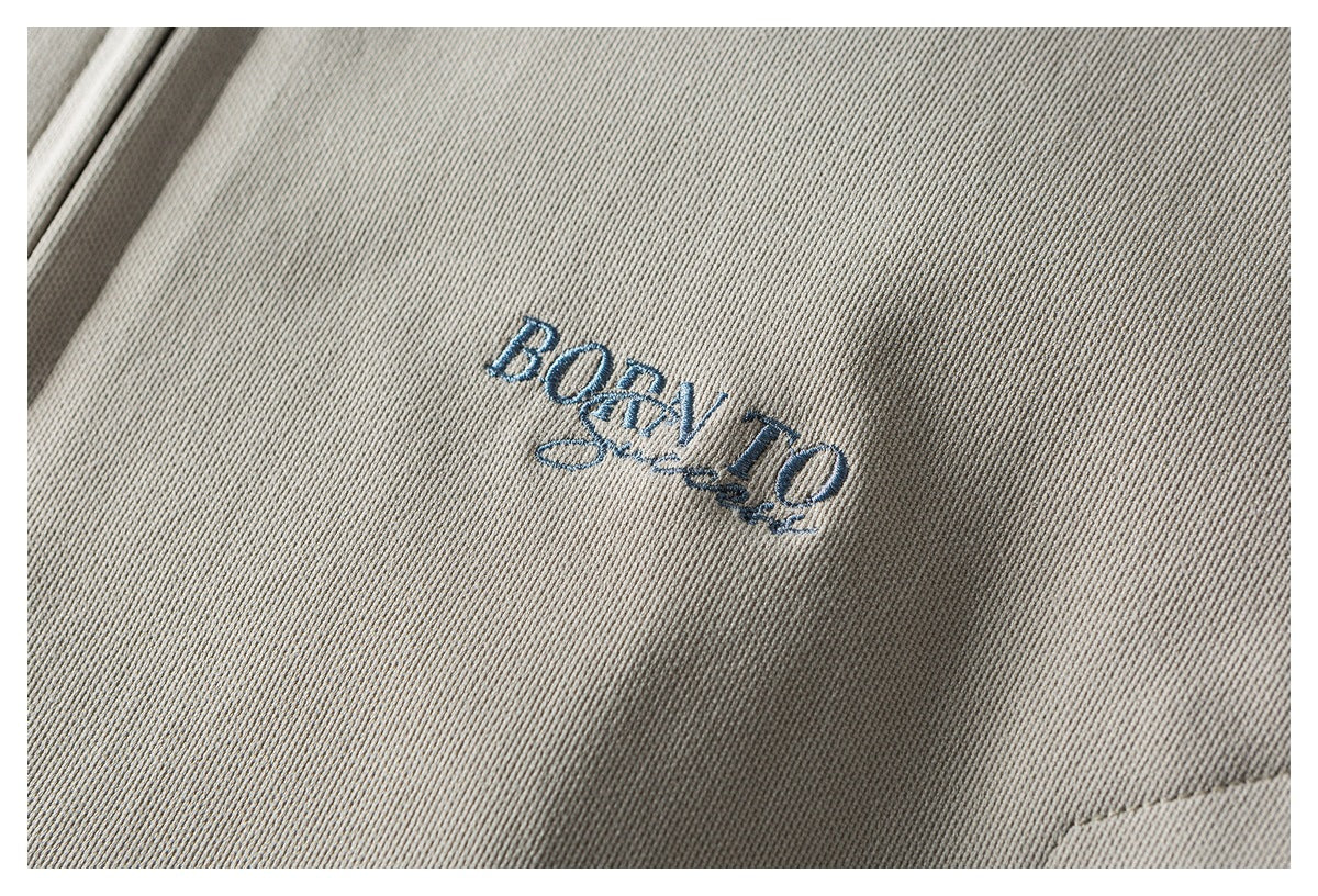 Close-up of blue embroidered lettering on the beige jacket.