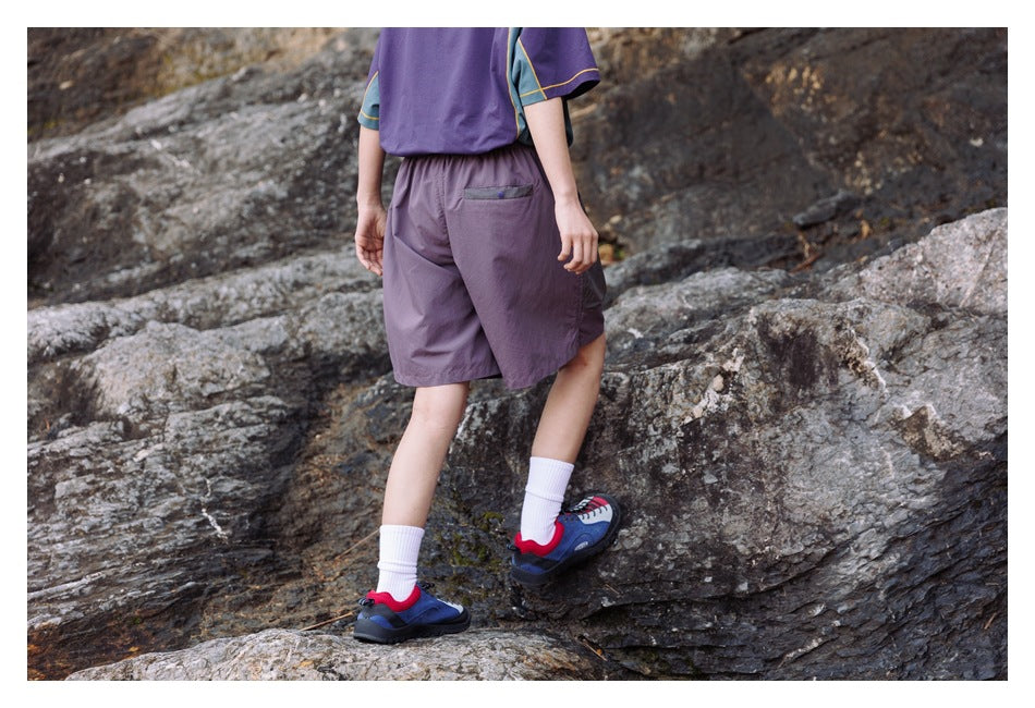 Rear view of a model wearing purple shorts with a small back pocket while standing on rocks.