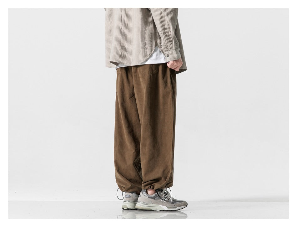 Rear view of a model wearing loose brown trousers with adjustable drawcord hems.