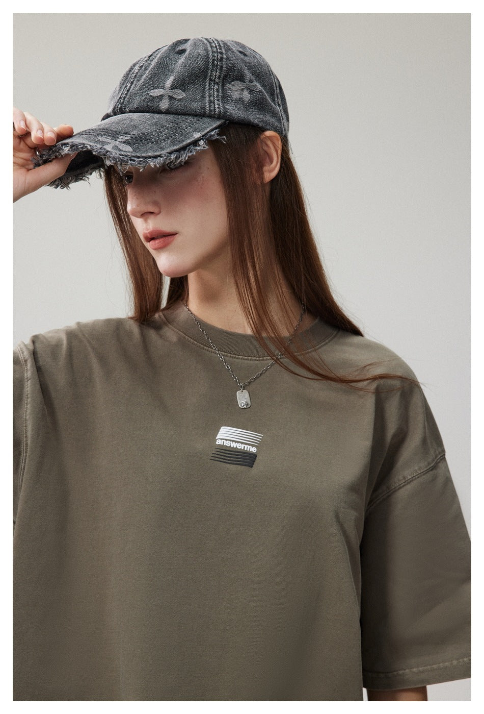 Close-up of a woman in an olive green T-shirt showing the chest graphic, dropped shoulder and washed denim cap