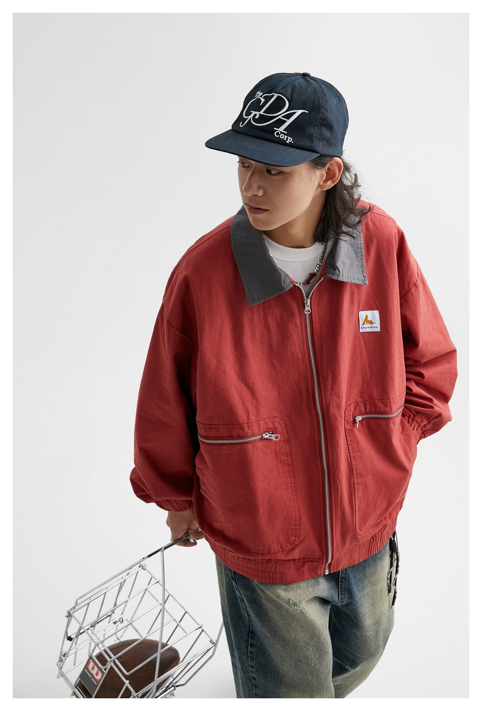 Model wearing a rust-red zip jacket with gray collar, roomy sleeves, and two large zippered pockets.
