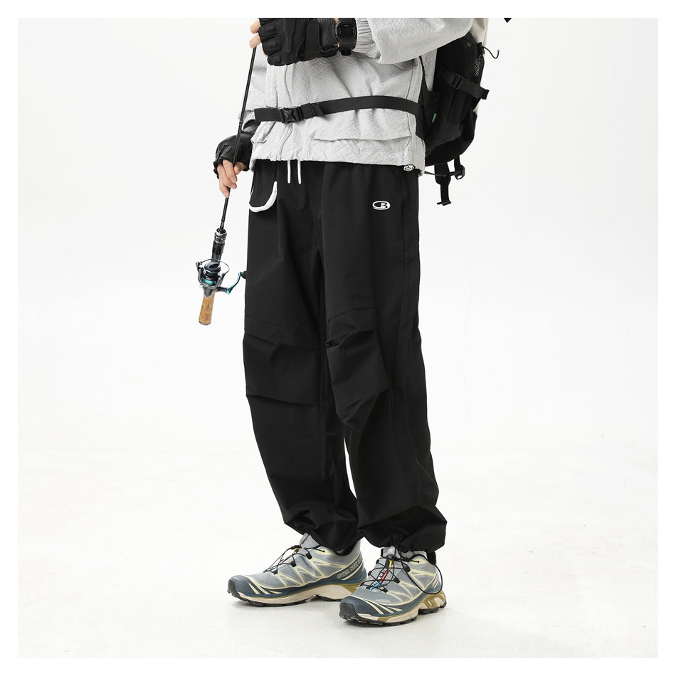 Cropped model wearing black loose cargo pants with layered pockets, paired with a light jacket and hiking shoes.