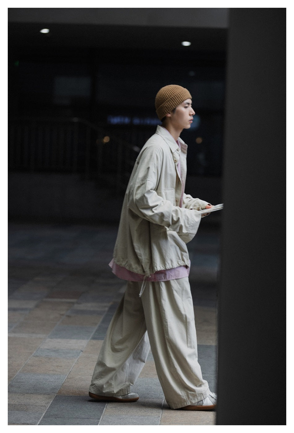 Model in a light gray oversized button-front jacket, pink striped shirt, and wide-leg trousers, shown in side profile.