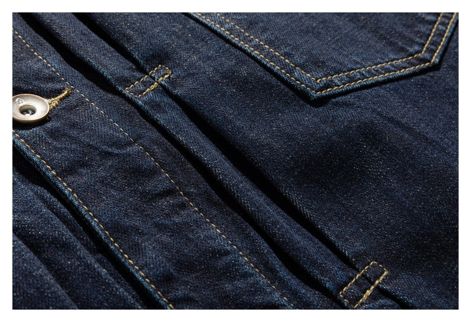 Close-up of dark indigo denim jacket with a chest pocket, button, and golden contrast stitching.
