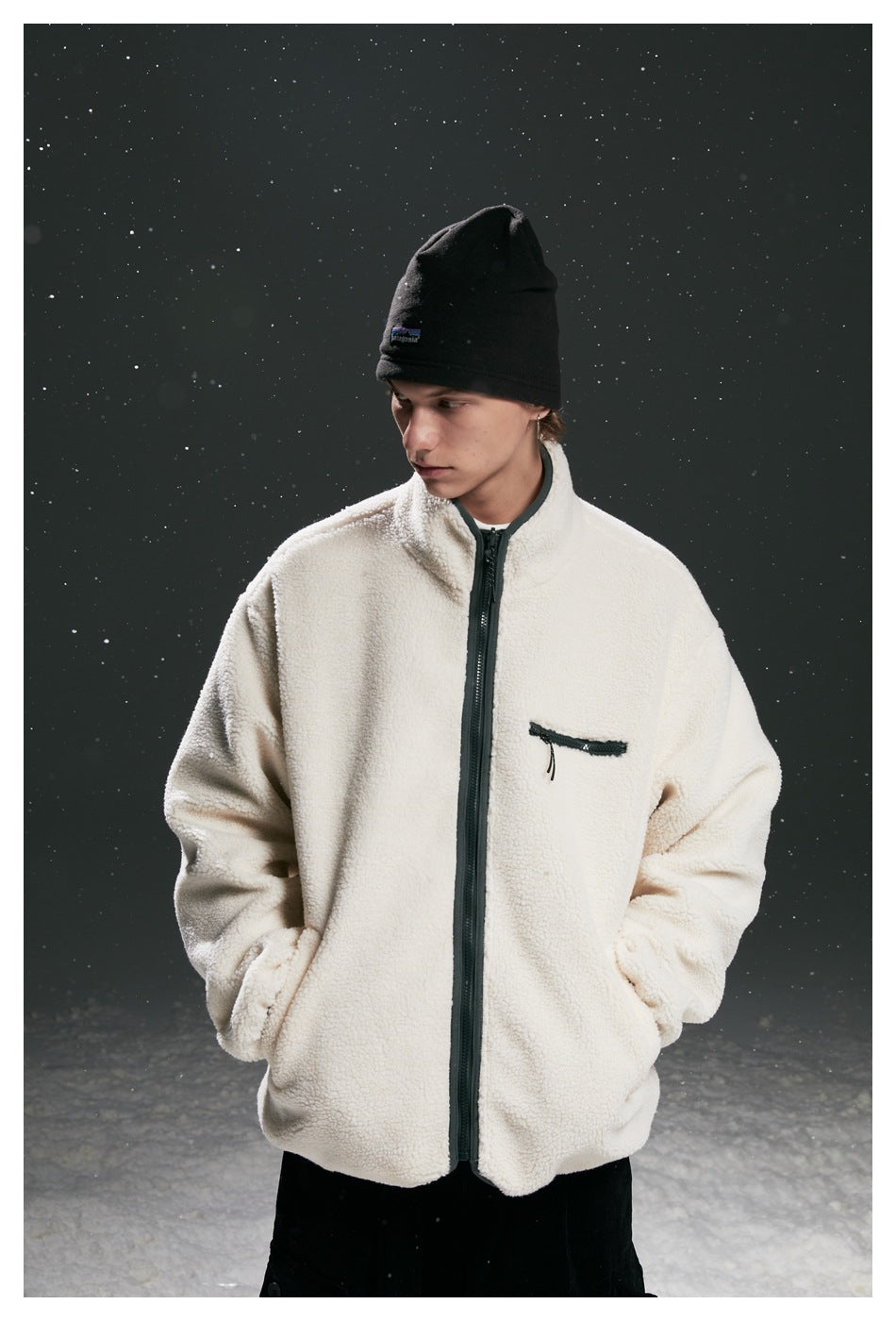 Model wearing a cream fleece zip jacket with dark trim, a chest zip pocket, black beanie, and black pants.