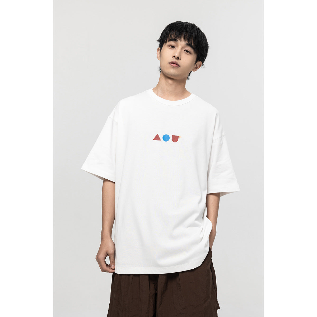 Front view of a model in a white oversized T-shirt with small red and blue geometric chest graphics.