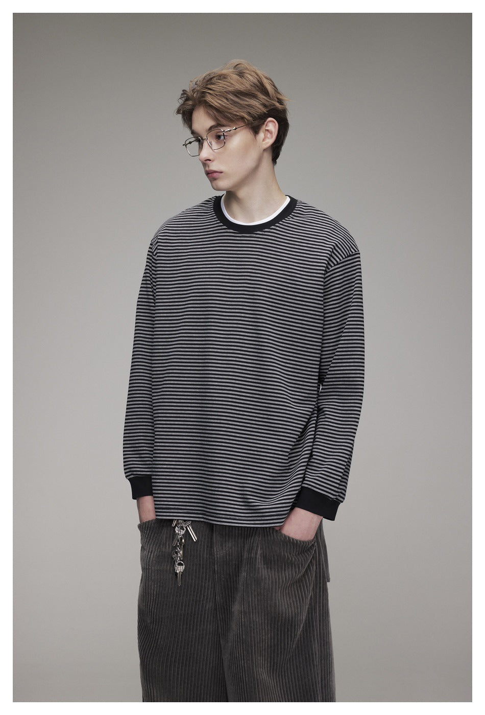 Front view of a model wearing an oversized black long-sleeve top with fine gray horizontal stripes and black ribbed trim.