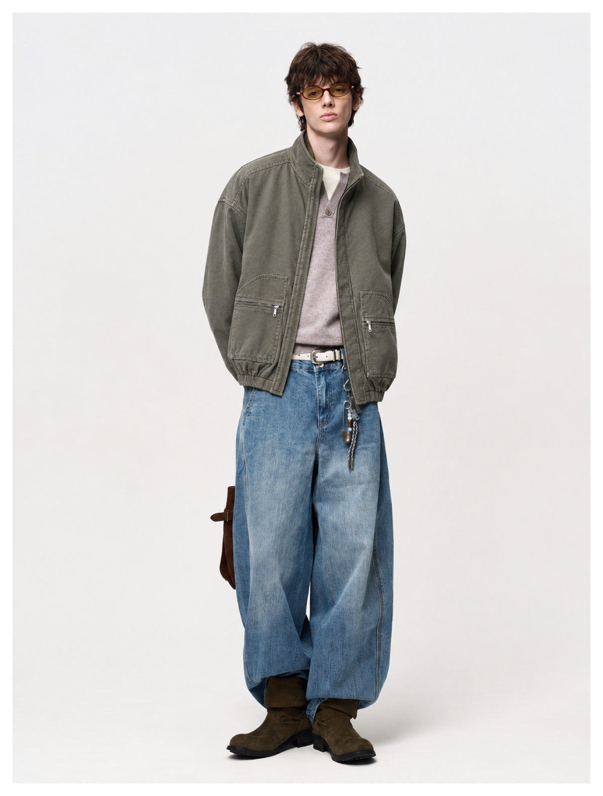 Model wearing army green jacket open over a lavender knit top with wide blue jeans and brown boots