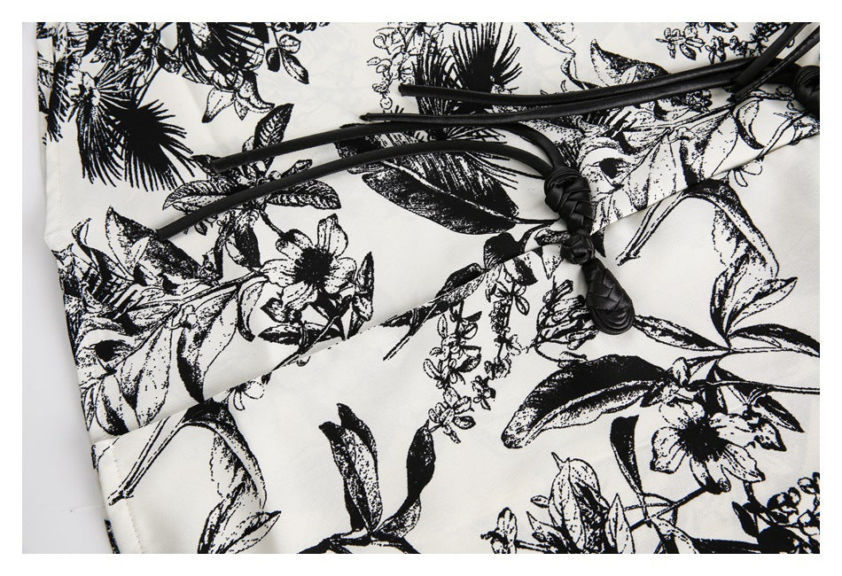 Close-up of an ivory garment with a black botanical print and a black cord tie finished with knotted ends.