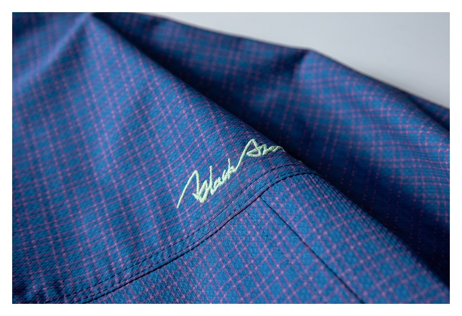 Close-up of pale embroidered script on navy and purple plaid fabric.