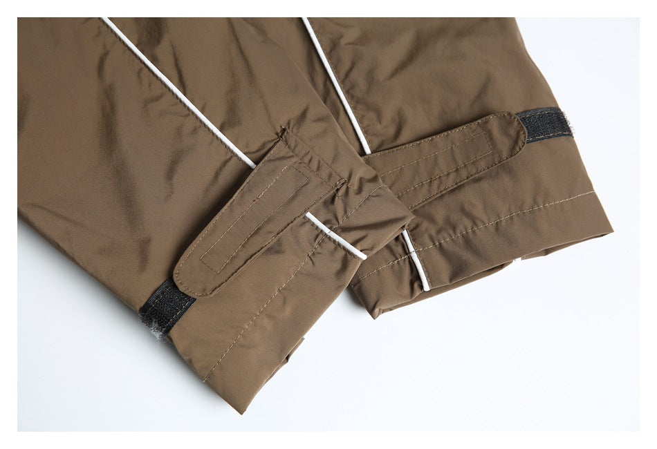 Close-up of a brown jacket sleeve cuff with white piping, stitched adjustment tabs, and black hook-and-loop patches.