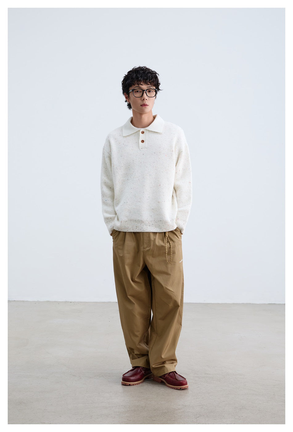 Full-length front view of a model wearing an ivory flecked knit polo sweater and loose tan trousers.