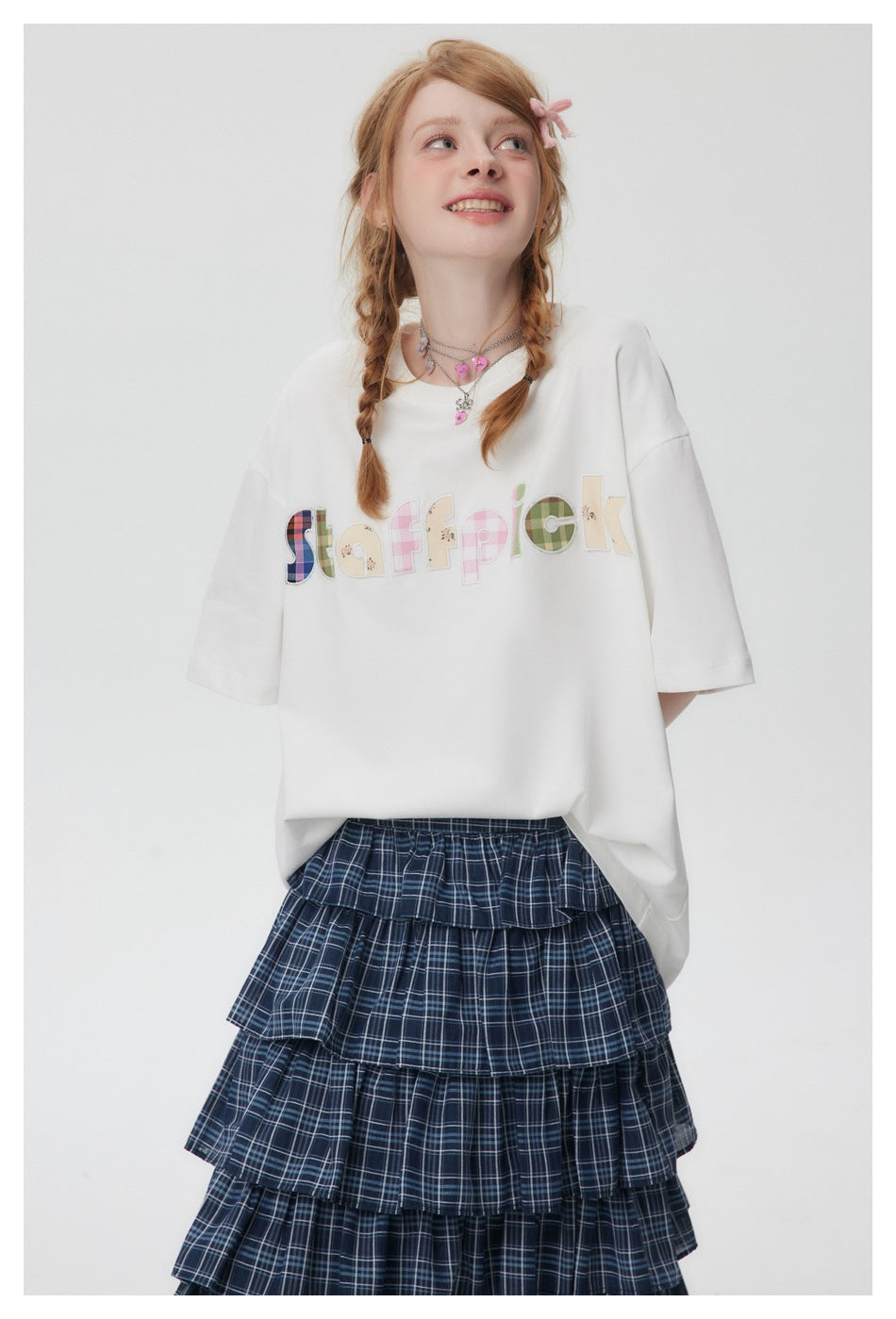 Close-up of a model wearing a white T-shirt with plaid, gingham and floral appliqué lettering on the chest