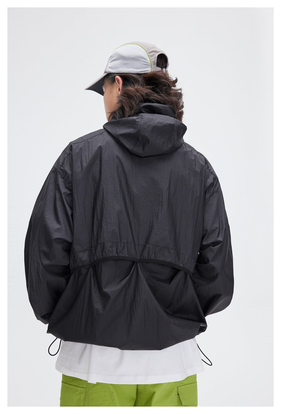 Back view of a model wearing a black hooded jacket with a large hood and lime-green shorts.