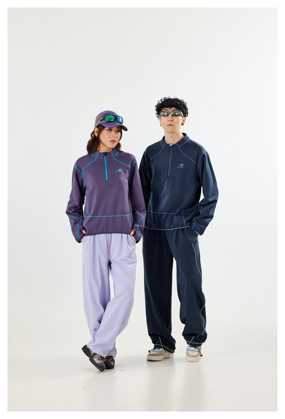 Two models wearing purple and navy quarter-zip pullovers with contrasting seam piping and loose pants.