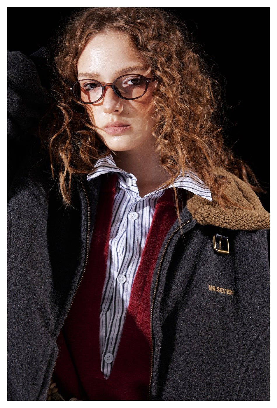 Close view of a model in a charcoal jacket with a tan fleece collar, layered over a red sweater and striped shirt.