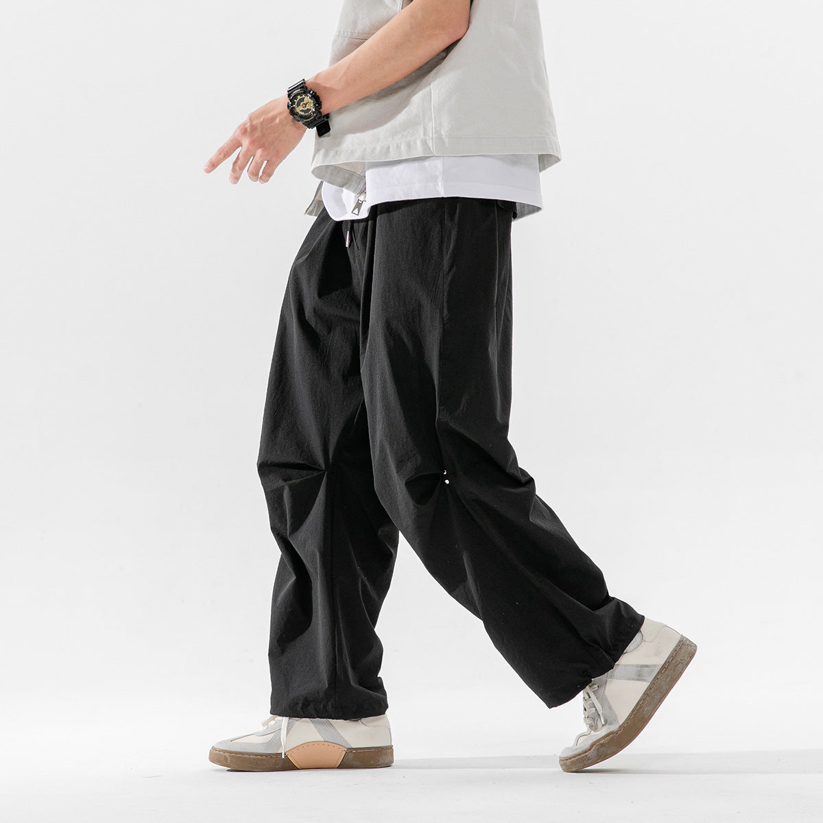 Side view of a model walking in loose black drawstring trousers with wide legs.