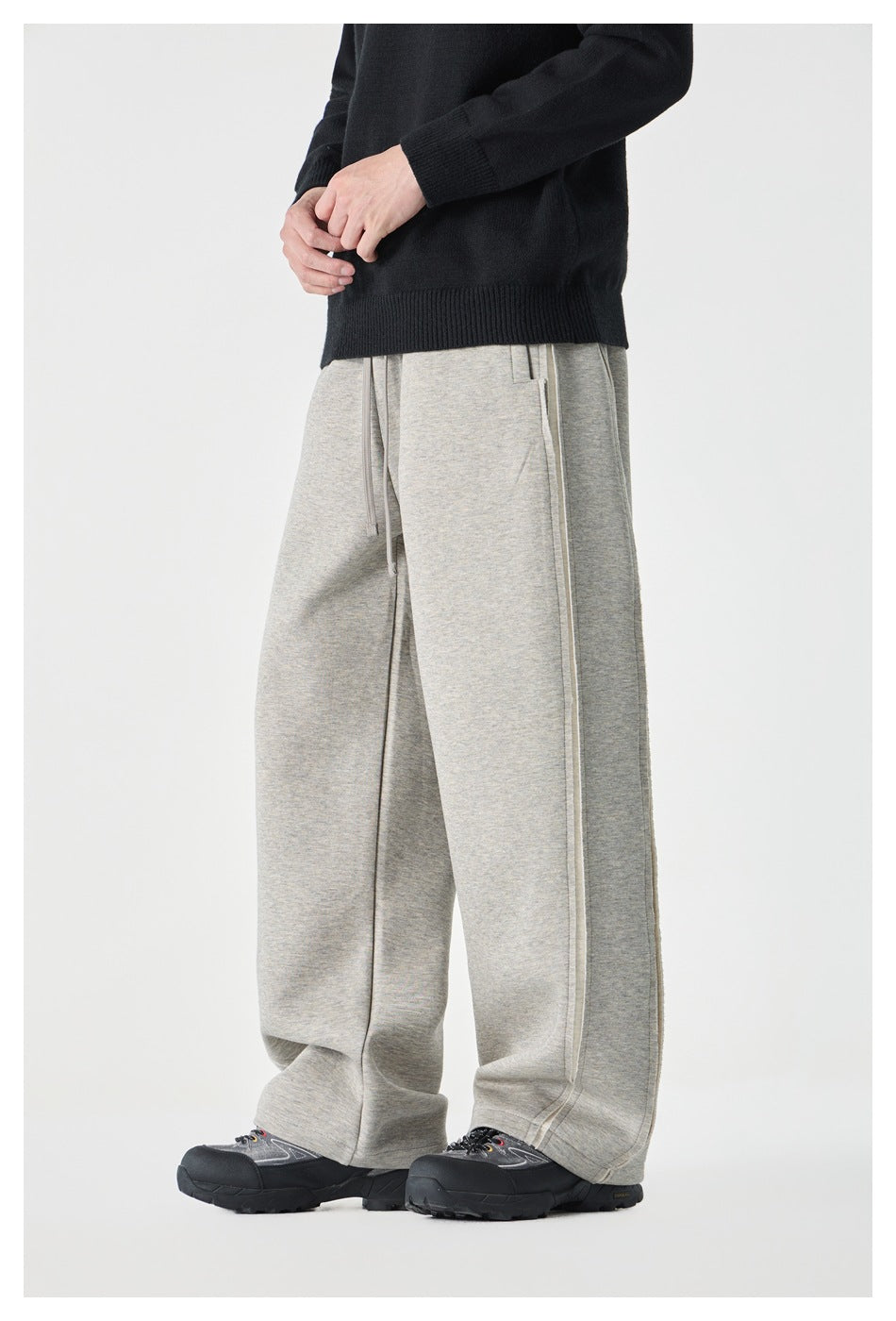 Side view of model wearing light gray wide-leg sweatpants with side seam detail, black sweater and dark sneakers