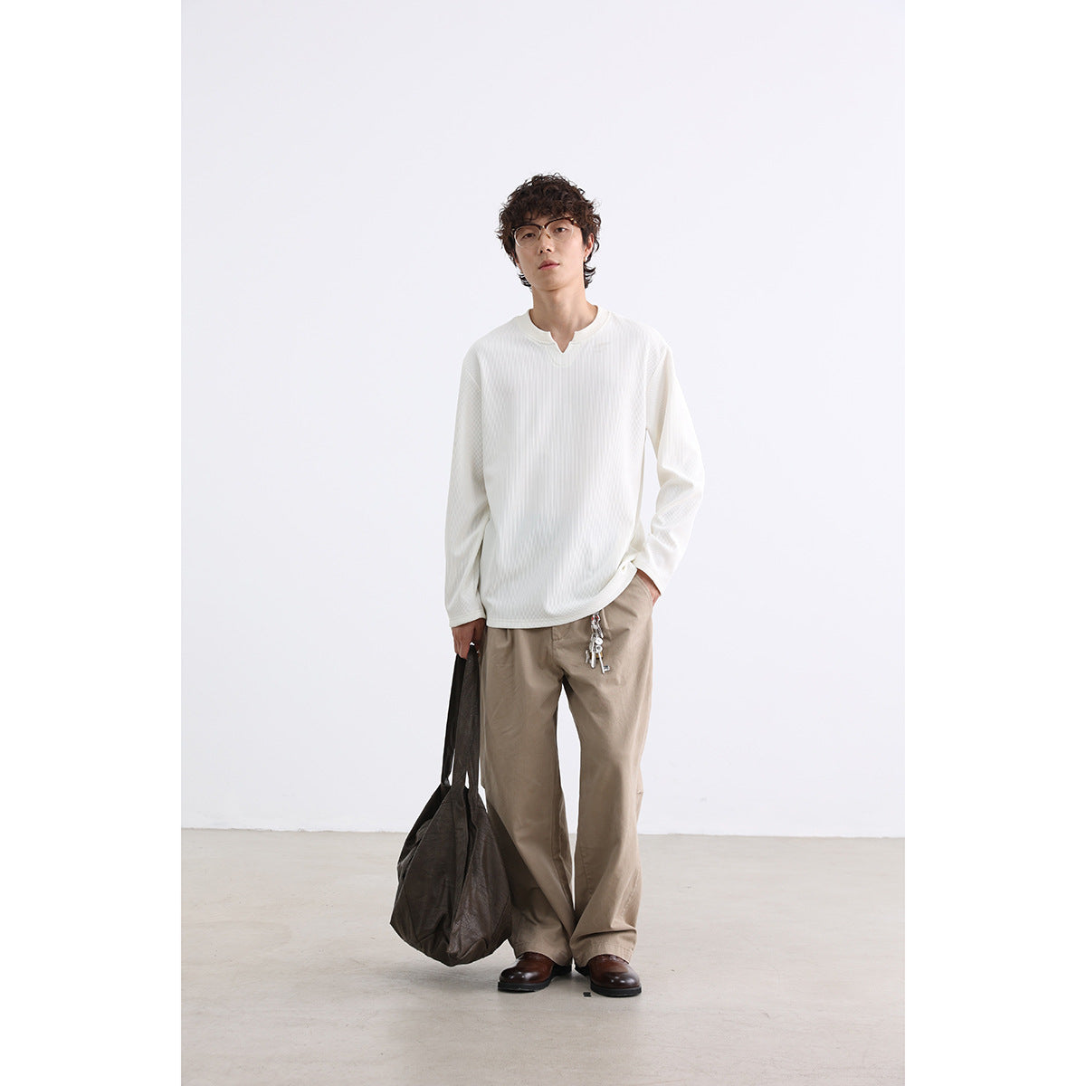 Model wearing an ivory long-sleeve ribbed shirt with a notched neckline and loose taupe trousers.