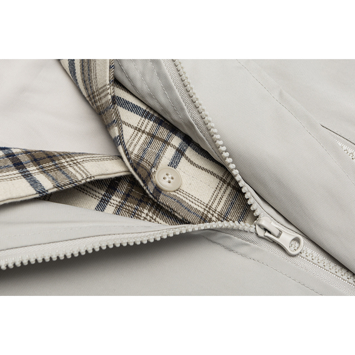 Close-up of a light gray jacket zipper and button with beige, brown, and navy plaid trim.