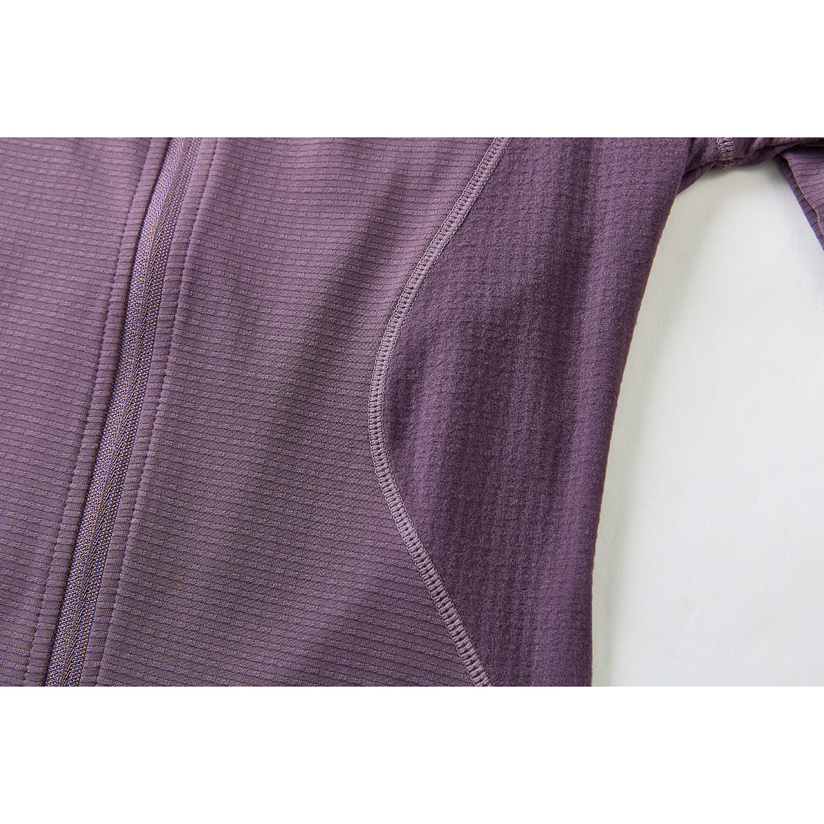 Close-up of the purple jacket's front zipper and curved side panel stitching.