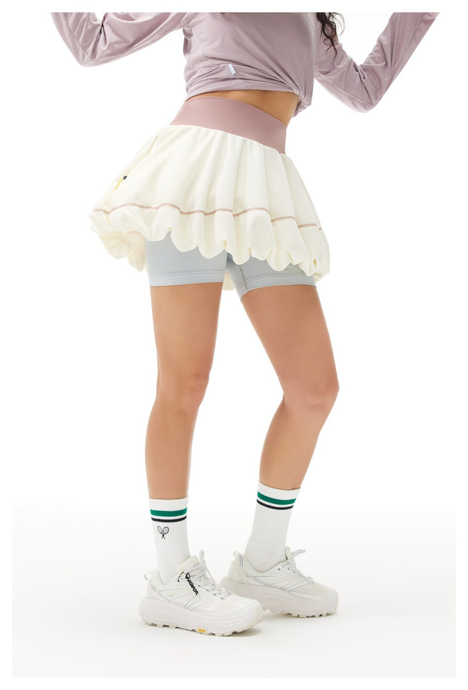 Rear view of a model wearing a cream bubble tennis skirt with dusty pink waistband and pale gray built-in shorts.
