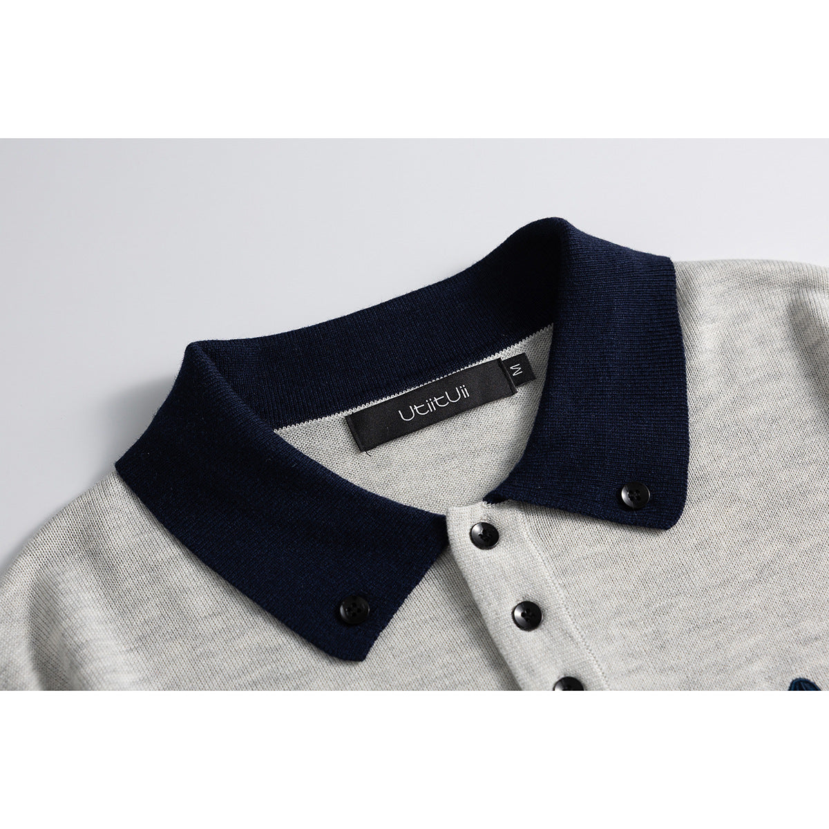 Close-up of a light gray knit polo collar with navy trim, black buttons, and an inner neck label.
