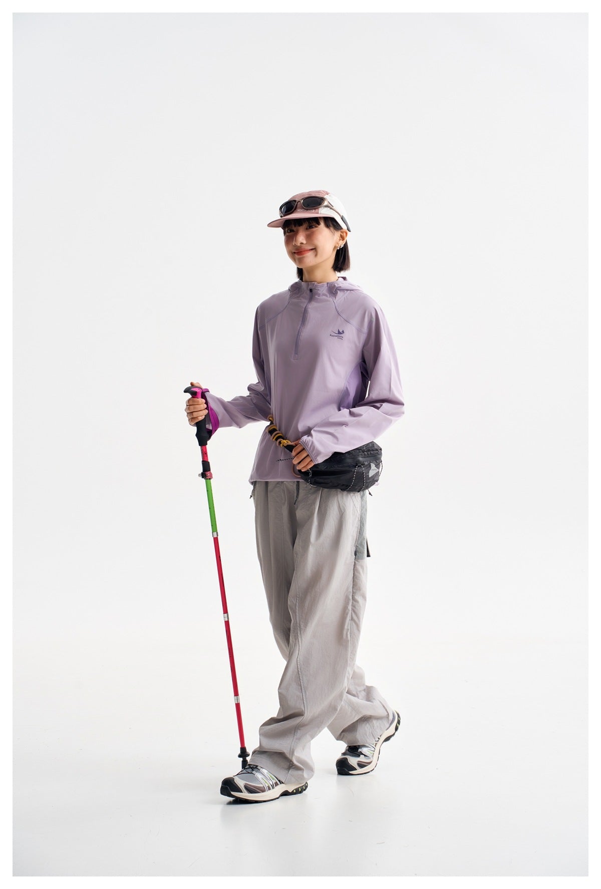 Model wearing a light lavender hooded pullover and loose light gray pants, shown in a three-quarter pose with a trekking