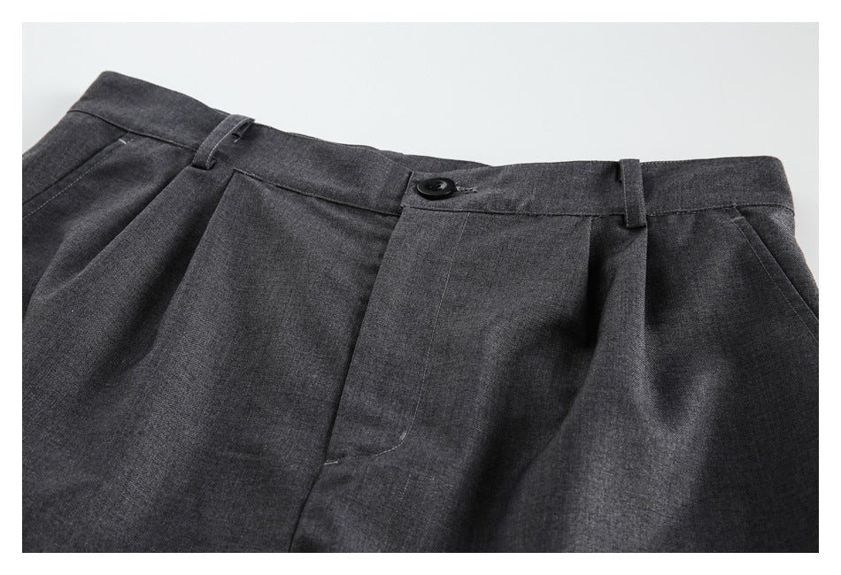 Close-up of charcoal gray shorts showing the waistband, belt loops, button, pleats and front pocket opening.