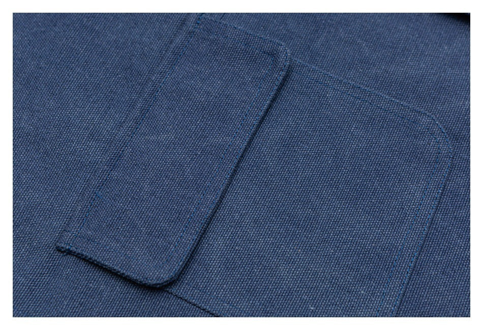 Close-up of a flap pocket on blue woven fabric, showing dark stitching and a brass-tone snap.