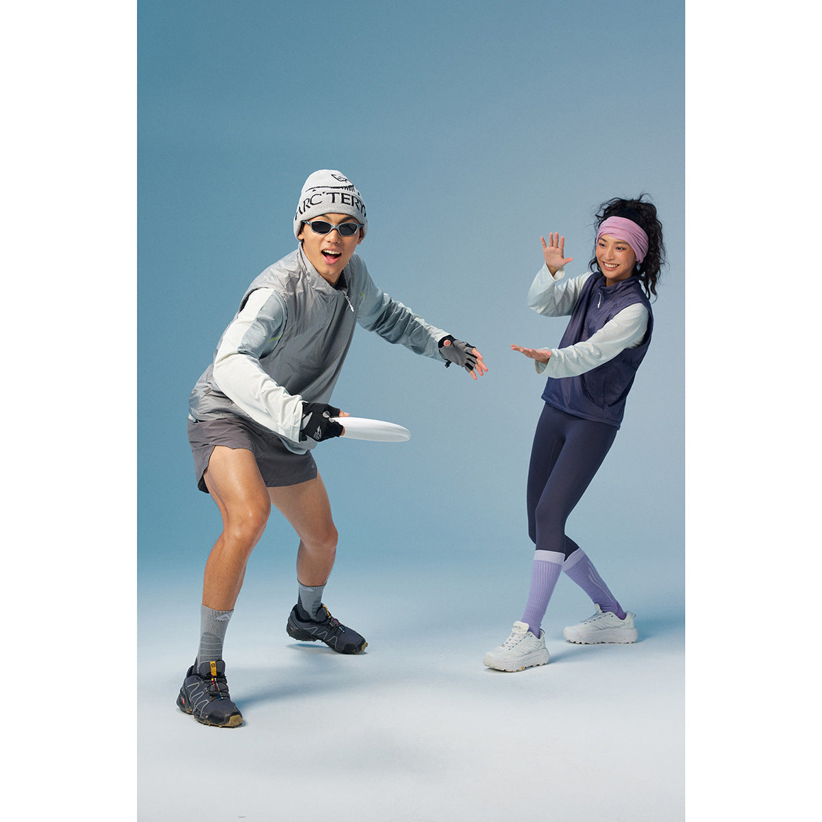 Two models in athletic layers: a man wears a gray pullover and shorts, while a woman wears a navy vest and leggings.