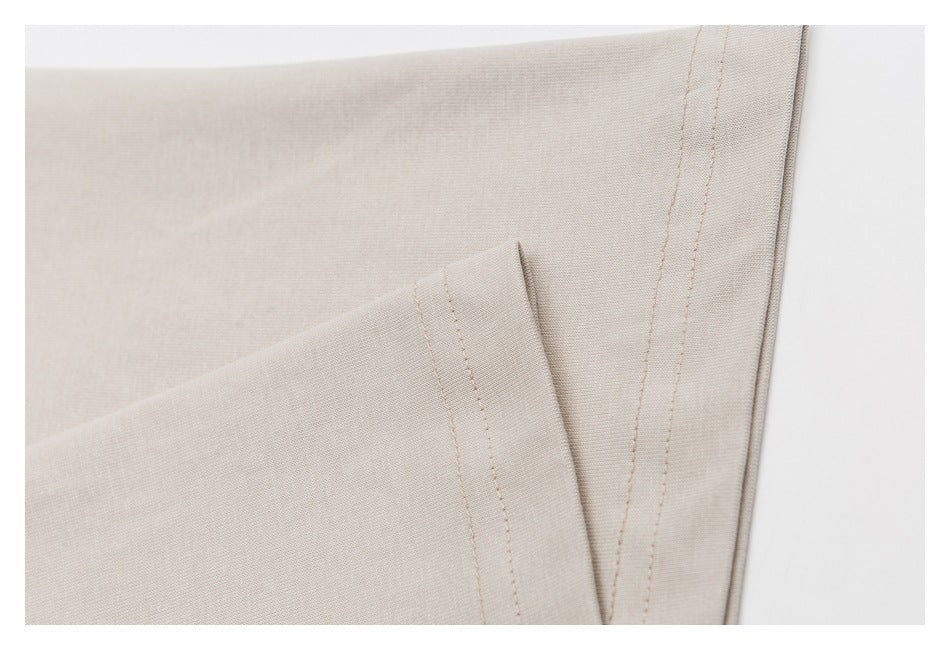 Close-up of beige T-shirt fabric showing a short-sleeve hem and double-stitched side seam.