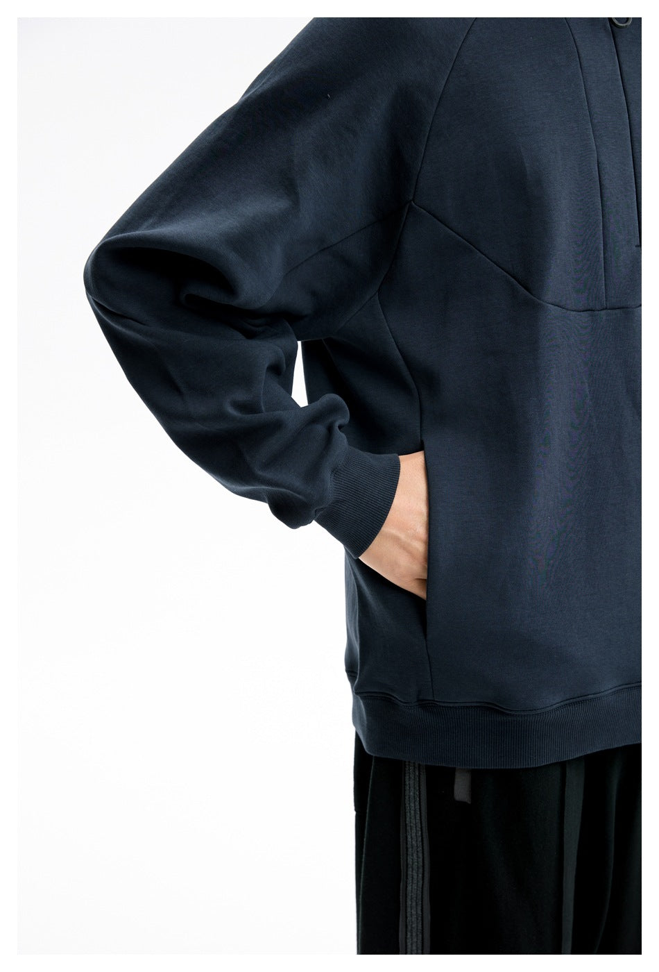 Close-up of the dark navy sweatshirt's raglan sleeve, curved seams, ribbed cuff, and side pocket.
