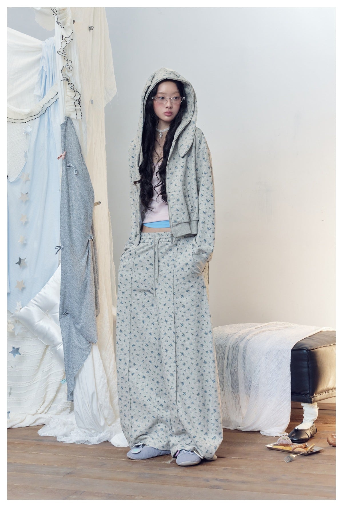 Model wearing gray floral zip hoodie with hood up and bunny ears, with matching floral wide-leg pants, full-length view