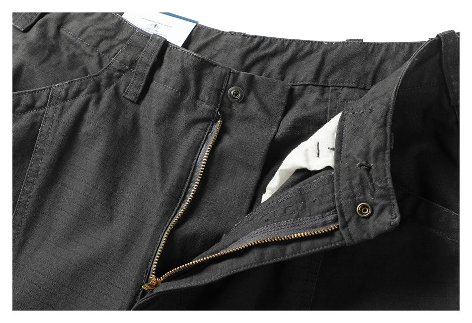 Close-up of charcoal trousers with the waistband and front fly unfastened, showing the brass zipper.