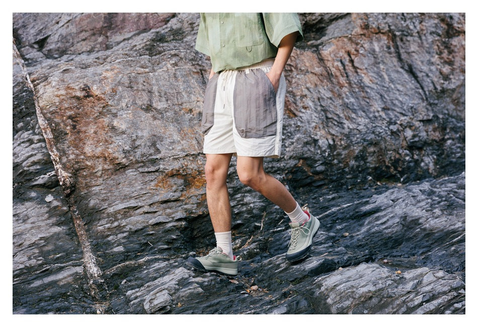 Three-quarter front view of a model wearing ivory shorts with oversized gray pockets on rocky terrain.