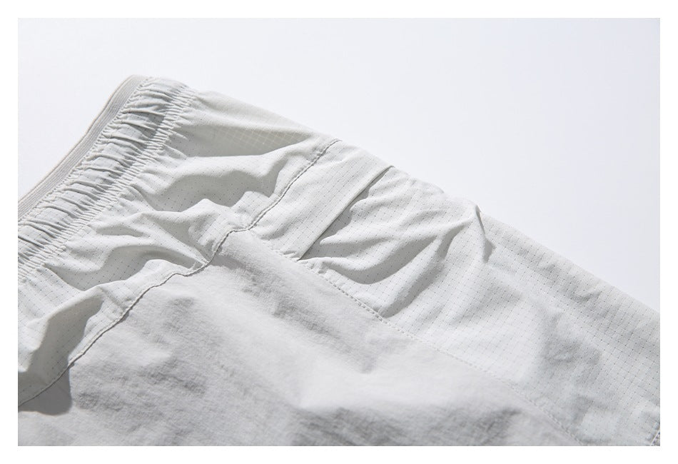 Close-up of pale gray shorts showing a gathered elastic waistband, tiny grid pattern, and stitched panel seams.