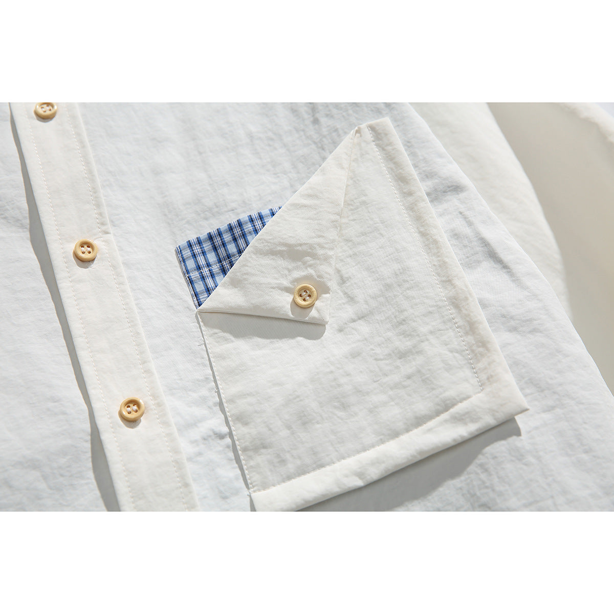 Close-up of an off-white shirt pocket with a buttoned flap and blue plaid trim, beside the button placket.