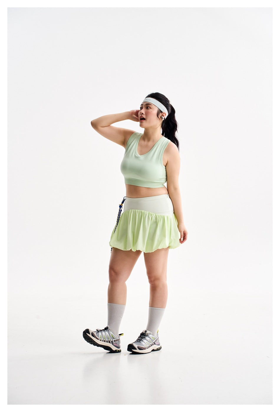 Three-quarter view of a model in a pale mint crop top and light green bubble-hem skirt, holding a frisbee.