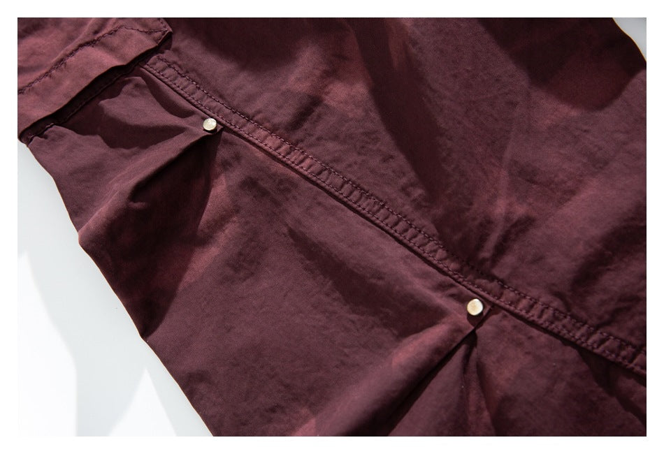 Close-up of burgundy cargo pants showing a stitched leg seam, gathered fabric and small metal rivets.