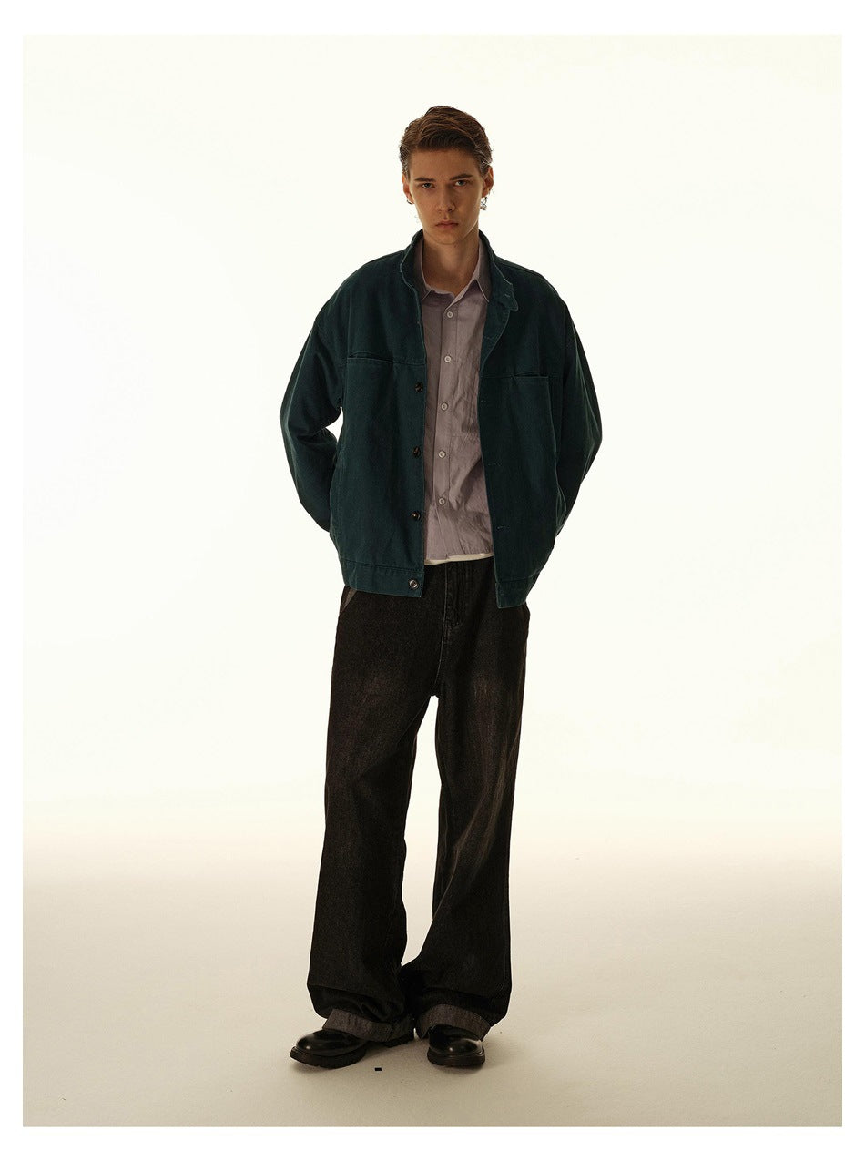 Full-length front view of a model in a dark teal jacket, mauve shirt, loose black trousers and black shoes.