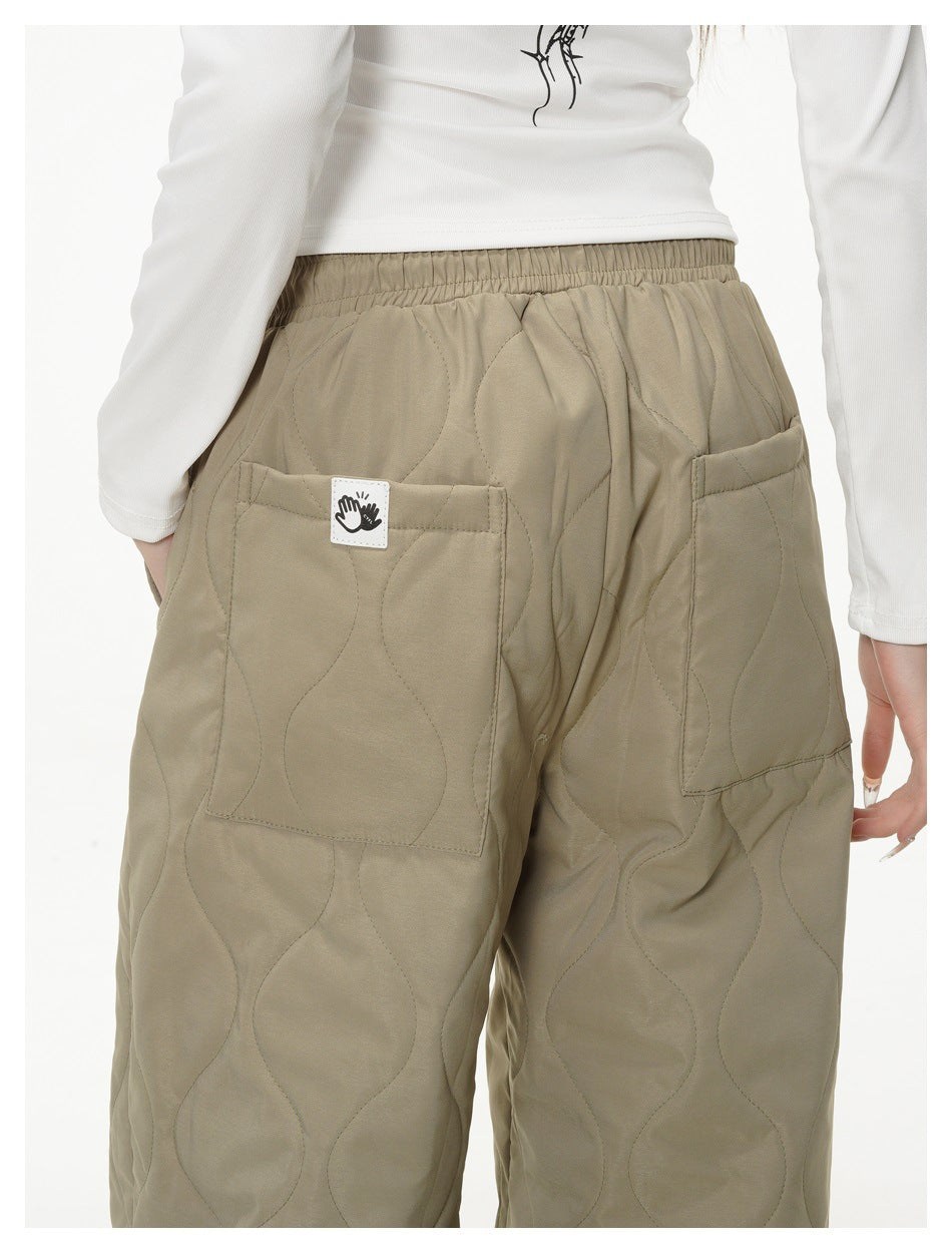 Close-up rear view of taupe quilted pants with an elastic waistband, two patch pockets and a small fabric label.