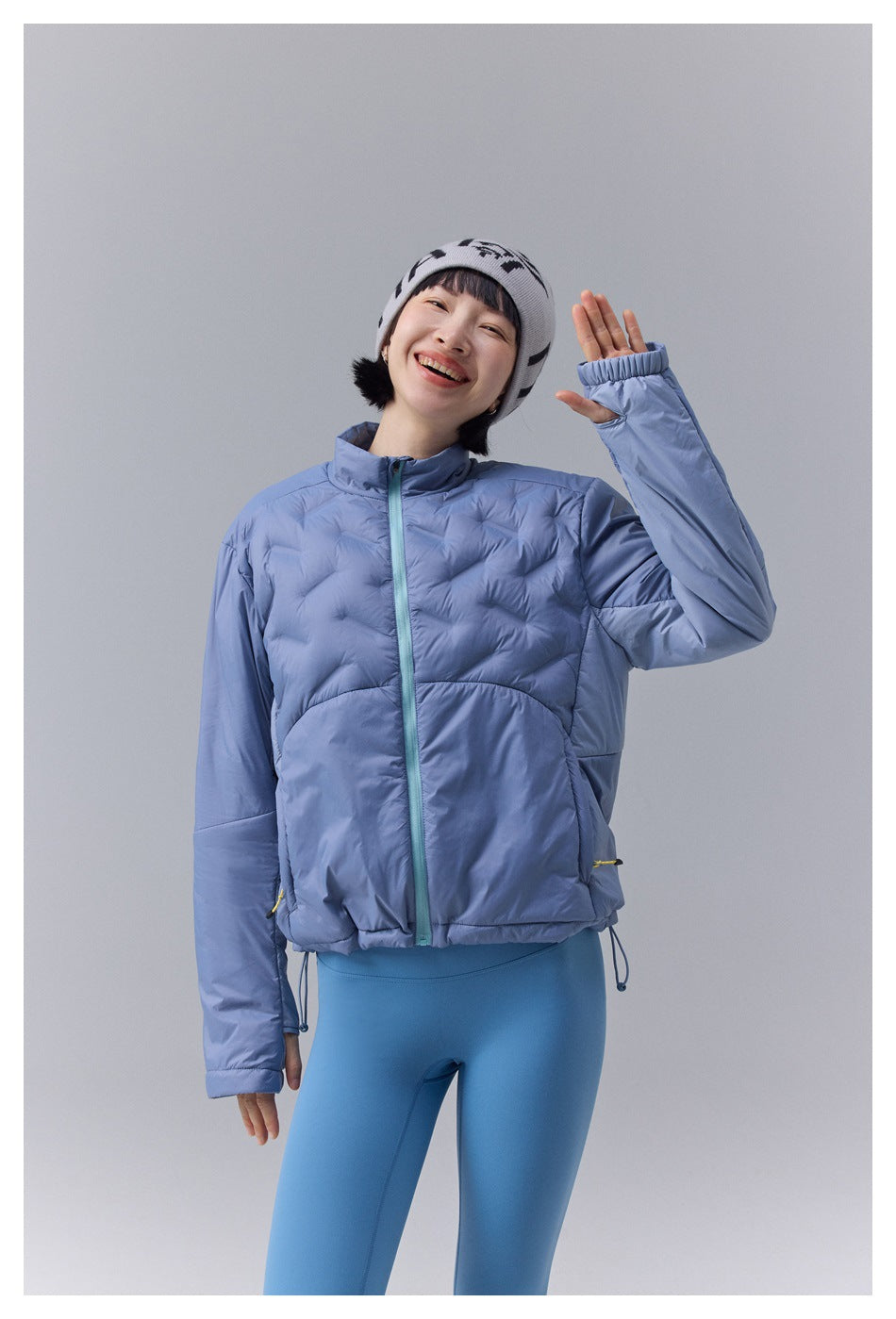 Model wearing a light blue quilted jacket zipped to the collar, with elastic cuffs and adjustable hem cords.